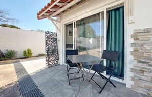 Eine Terrasse mit Tisch und Stühlen, eine Glasschiebetür und ein schmiedeeiserner Zaun.