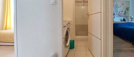 Ett tvättrum med tvättmaskin, torkställning och en duschkabin.