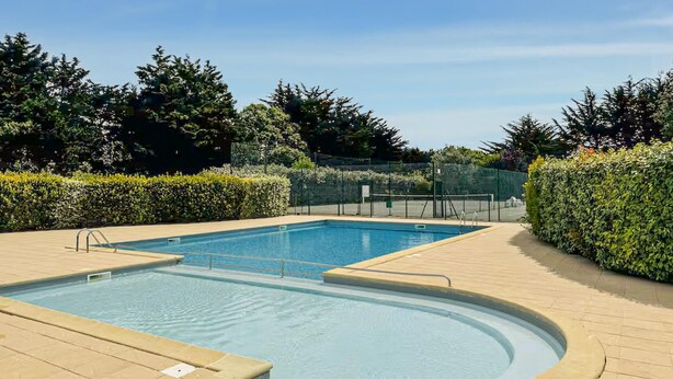 A rectangular swimming pool with a circular hot tub area, surrounded by a brick deck and bordered by hedges.