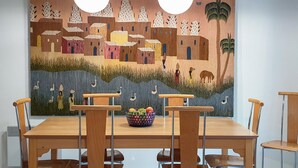 A dining area with a wooden table and chairs, a mural on the wall, and a bowl of fruit on the table.
