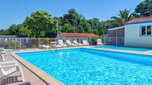 En swimmingpool med liggestole, et hegn og en bygning med rødt tag.