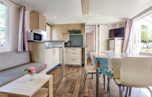 A compact kitchen with a microwave, stove, and sink. There is a dining area with a table and chairs. - Charmant Mobil-home piscine (Saint-Georges-de-Didon)