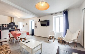 Ein Wohnzimmer mit Essbereich, einem an der Wand befestigten Fernseher und einem großen Fenster mit Vorhängen.