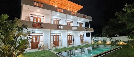 A two-story building with a swimming pool, multiple balconies, and a well-lit exterior.