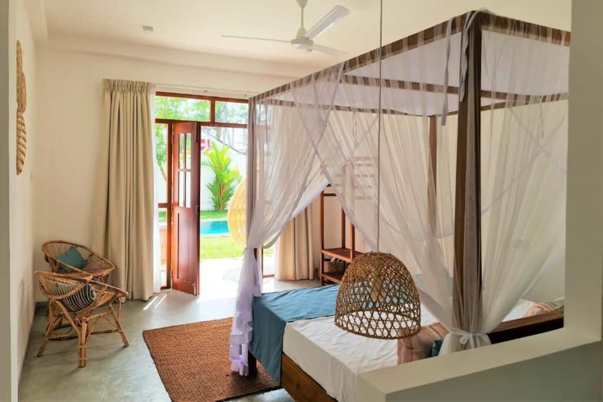 Quarto com cama, cadeira, ventoinha e vista para o exterior.