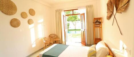 Habitación de hotel con dos camas, ventilador de techo, ventana con cortinas, muebles de mimbre y decoración en la pared.