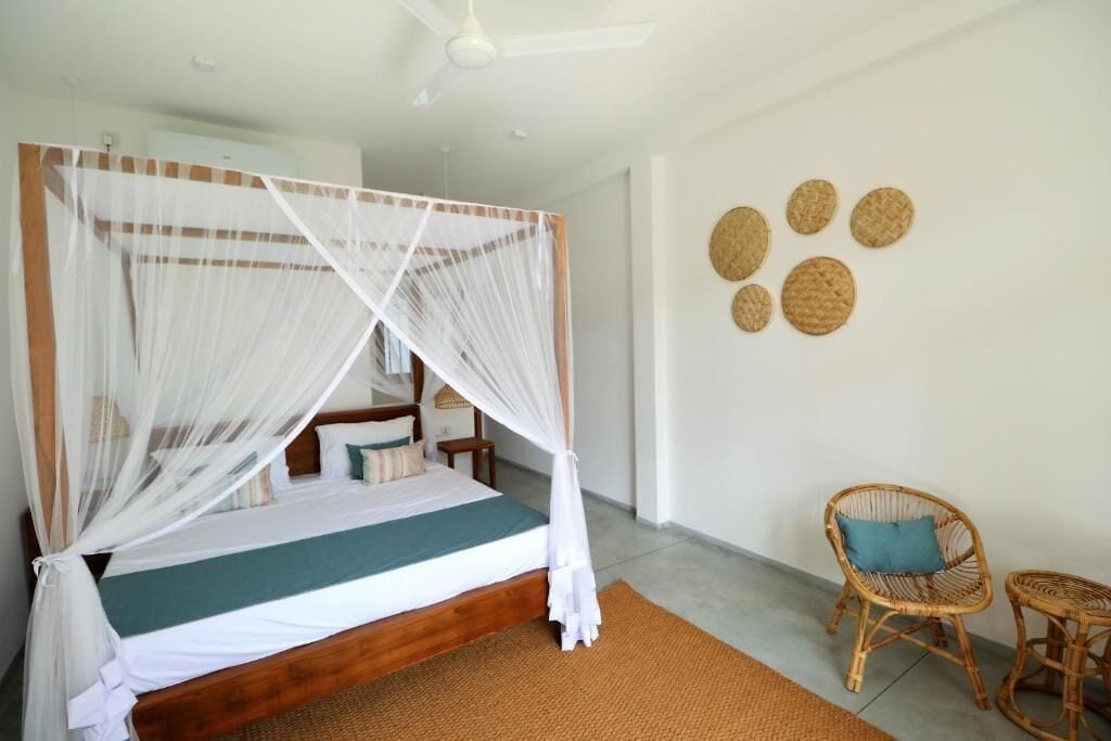 A bed with a canopy, a wicker chair, a small table, and wall decor.