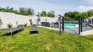 A backyard with a swimming pool, lounge chairs, and a fenced area. - Charmante maison avec piscine (Le Château-d'Oléron)