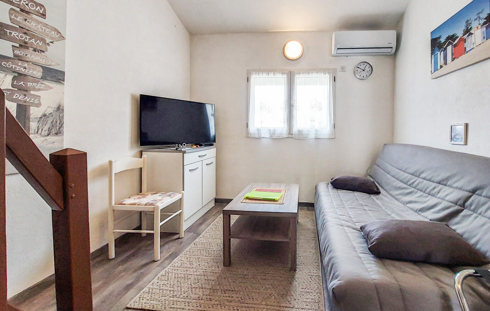 Una sala de estar con un sofá, un televisor, una mesita, una silla y una escalera.