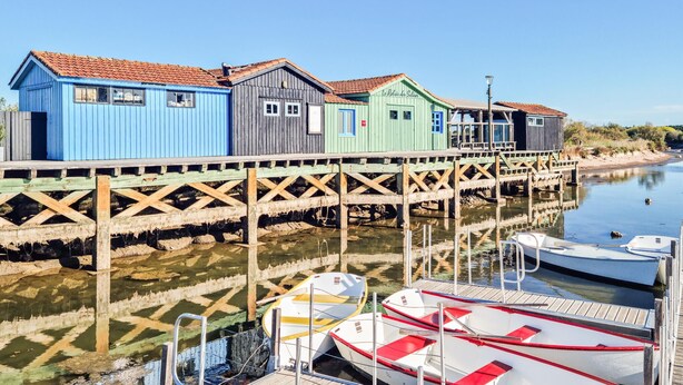 A wooden pier with colorful wooden buildings and boats docked at the end. - Charmante maison avec piscine (Le Château-d'Oléron)