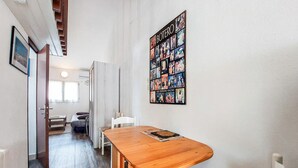 A room with a wooden dining table, a white chair, a bed with a headboard, a window, and a wall with a collage of photographs. - Charmante maison avec piscine (Le Château-d'Oléron)