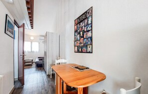Ein Zimmer mit einem Holzespeisetisch, einem weißen Stuhl, einem Bett mit Kopfteil, einem Fenster und einer Wand mit einer Collage aus Fotos.