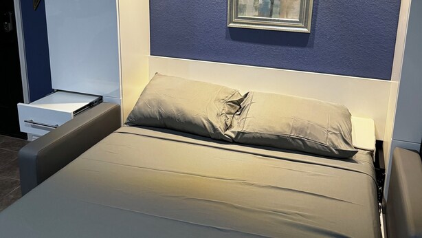 A modern bedroom with a bed, bedside tables, a framed artwork, and recessed ceiling lighting.