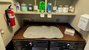 A laundry room with two washing machines, shelves with cleaning supplies, and a fire extinguisher.