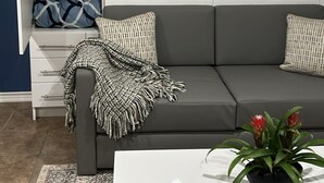 A modern living room with a grey sofa, white storage unit, and a coffee table with a plant.