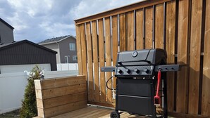 Una parrilla de barbacoa en una terraza de madera, con una valla de madera al fondo.