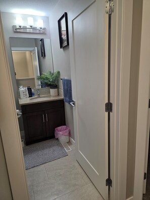 A bathroom with a sink, mirror, towel rack, and a trash bin. - Grand Stylish Home | TVs in Bedrm & Lvroom | Comfy mattresses |Garage park | BBQ (Regina)