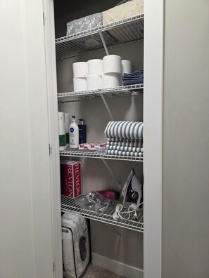A storage closet with shelves containing paper towels, cleaning supplies, and a vacuum cleaner. - Grand Stylish Home | TVs in Bedrm & Lvroom | Comfy mattresses |Garage park | BBQ (Regina)