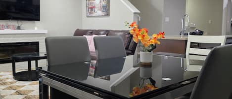 A modern dining area with a glass-top table, black chairs, and a vase with flowers.