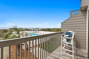 A wooden deck with a pool, white fence, and a bench with cushions.