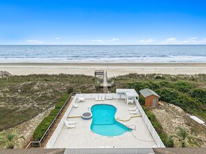 A pool area with lounge chairs, a small pool, and a view of the beach.
