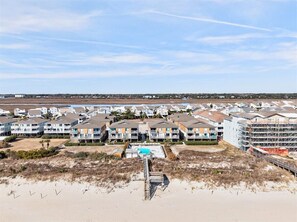 A coastal residential area with multi-story buildings, a swimming pool, and a beach in the foreground.