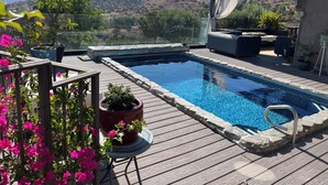Una piscina con vistas a montañas, un espacio de descanso techado y plantas en macetas.
