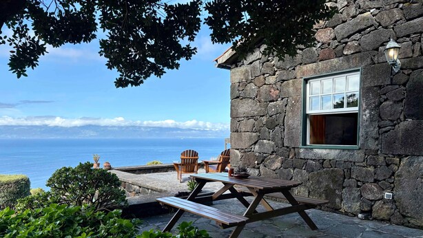 Ein Gebäude aus Stein mit einer Holzterrasse, einem Tisch und Stühlen.