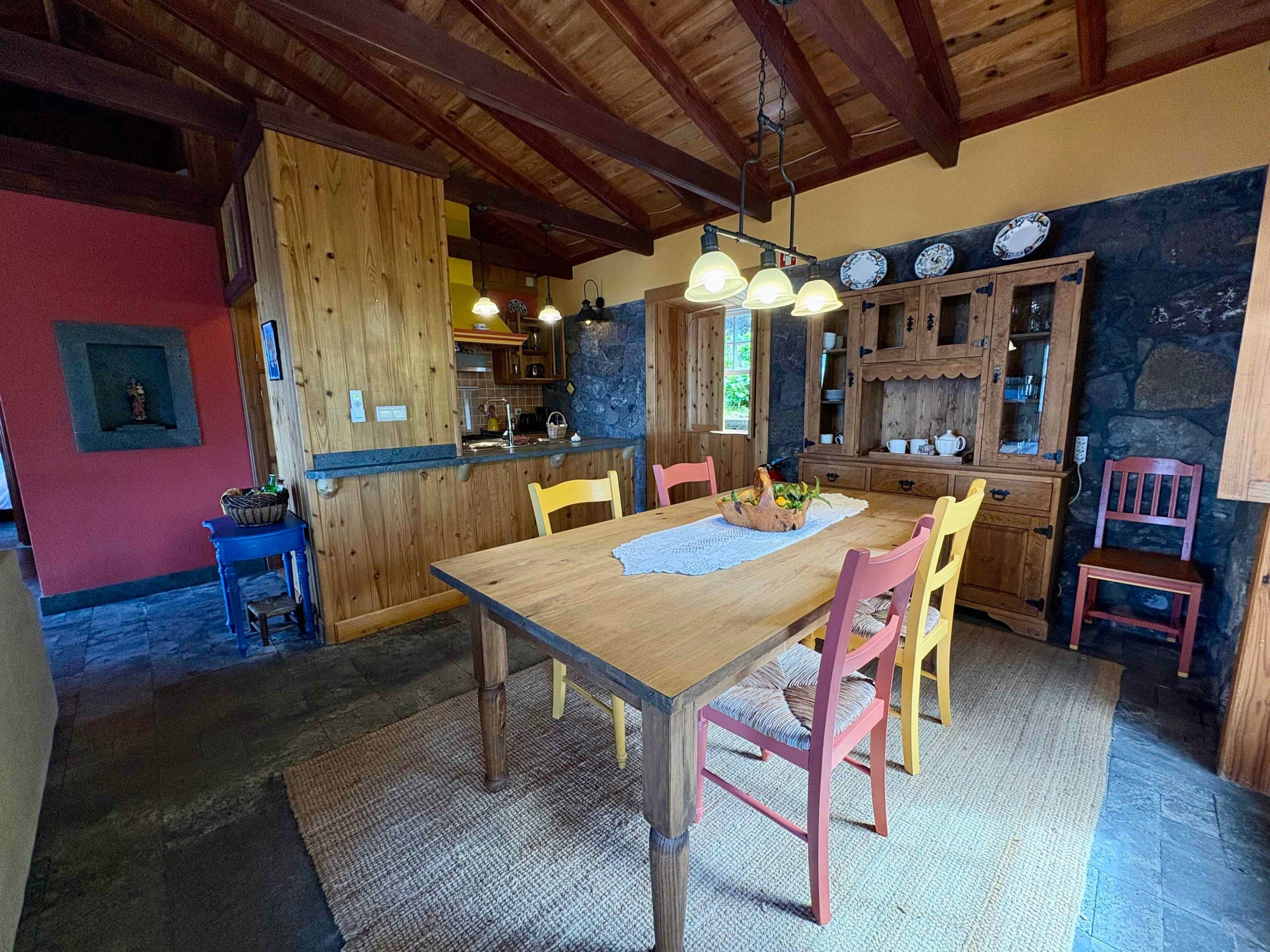 A rustic kitchen with wooden cabinets, a dining table with chairs, and a stone wall.