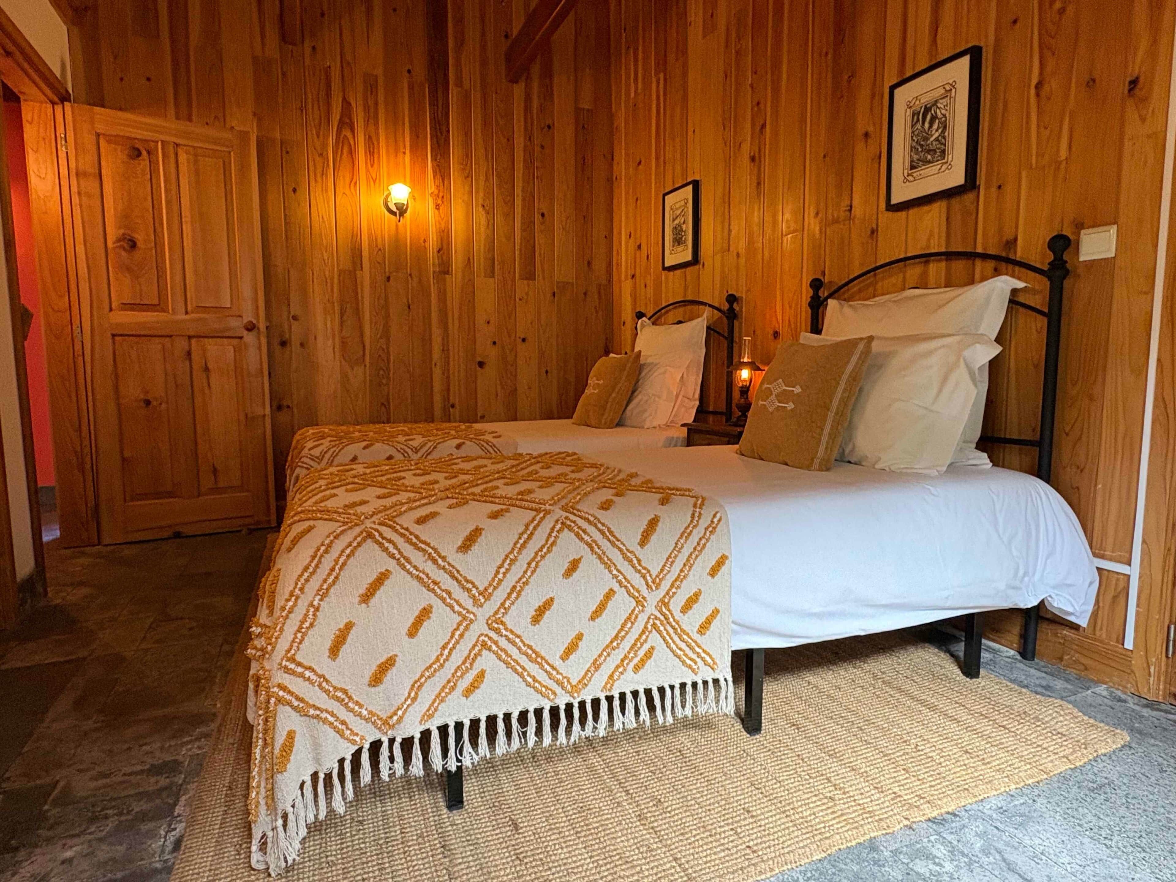 Una habitación con paneles de madera, una cama, una lámpara en la pared y una puerta.