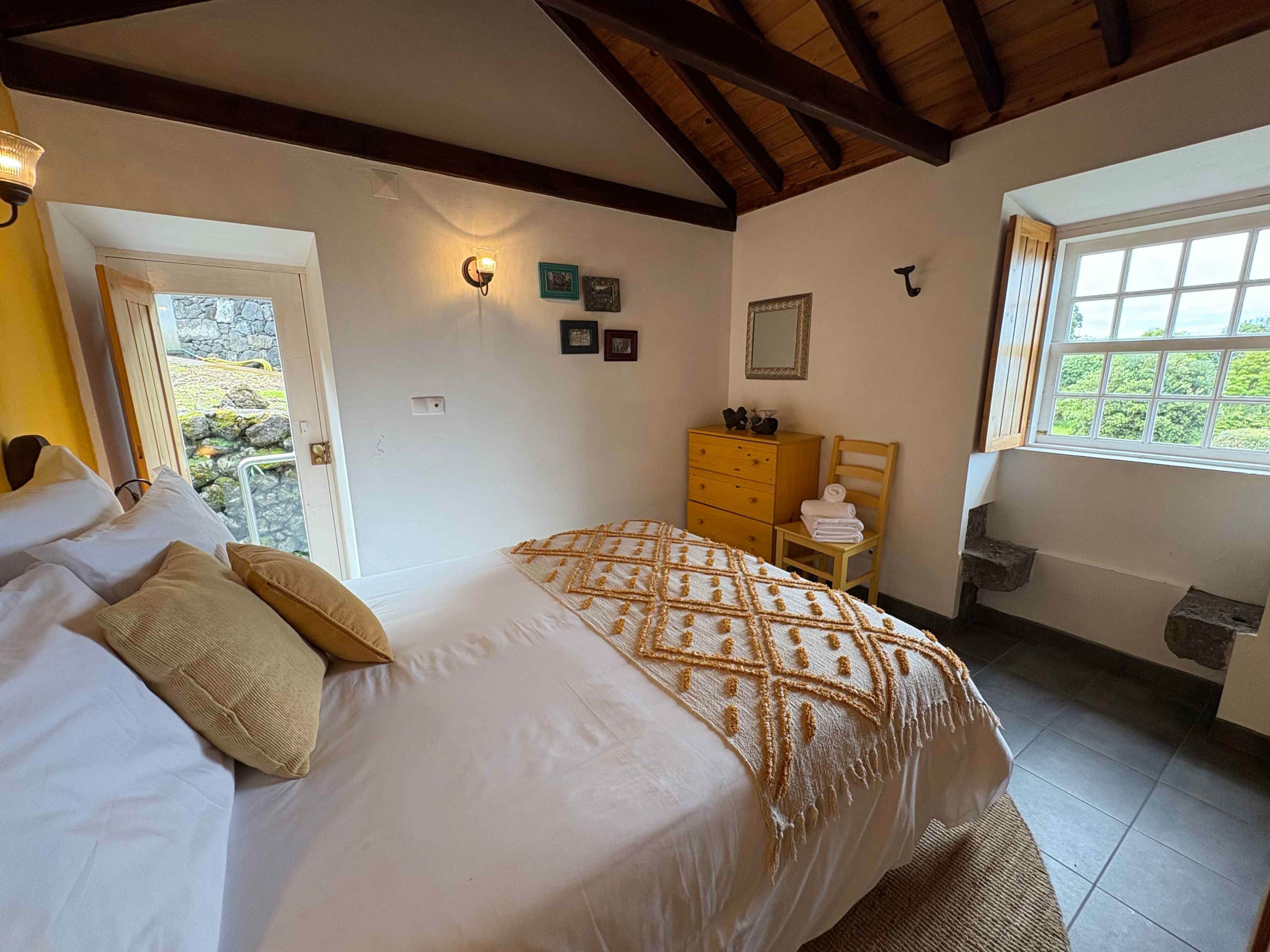 A bedroom with a bed, a dresser, a chair, a mirror, and a window with a view.