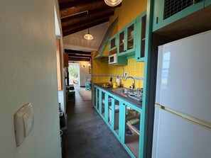 A narrow hallway with a kitchen area featuring teal cabinets, a white refrigerator, and a microwave.