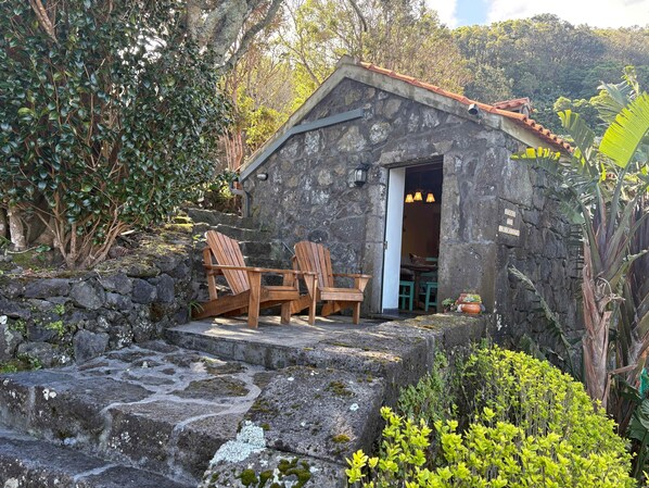 A stone building with a tiled roof, wooden chairs outside, and a stone staircase leading up to the entrance.
