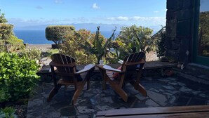 A patio with two wooden chairs and a table, overlooking a scenic view of the ocean and mountains. - Casa do Jardim (Santo Amaro)