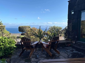 A patio with two wooden chairs and a table, overlooking a scenic view of the ocean and mountains. - Casa do Jardim (Santo Amaro)