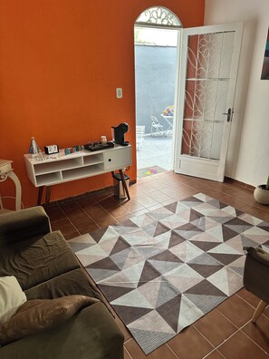 A living room with a sofa, a white console table with decorative items, a patterned rug, and a door leading outside. - House in Aparecida, SP, 5 to 10 minutes from the Basilica and 5 minutes from Porto Itaguaçu. (Aparecida)