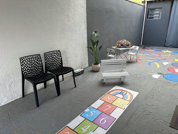 A paved outdoor area with a hopscotch game, two black chairs, a white bench, and a potted plant. - House in Aparecida, SP, 5 to 10 minutes from the Basilica and 5 minutes from Porto Itaguaçu. (Aparecida)