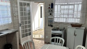 Une cuisine équipée d’une table à manger, de chaises, d’un réfrigérateur et d’une fenêtre avec un rideau.