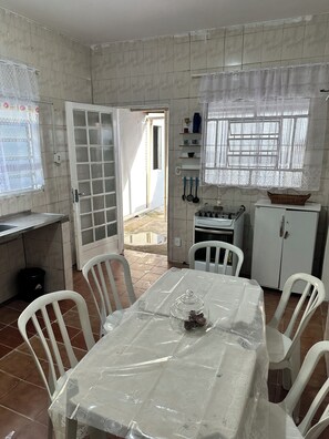 A kitchen with a dining table, chairs, a refrigerator, and a window with a curtain. - House in Aparecida, SP, 5 to 10 minutes from the Basilica and 5 minutes from Porto Itaguaçu. (Aparecida)