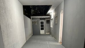 Un couloir étroit, dont le sol est recouvert de carreaux, mène à une porte surmontée d’un portail en métal.