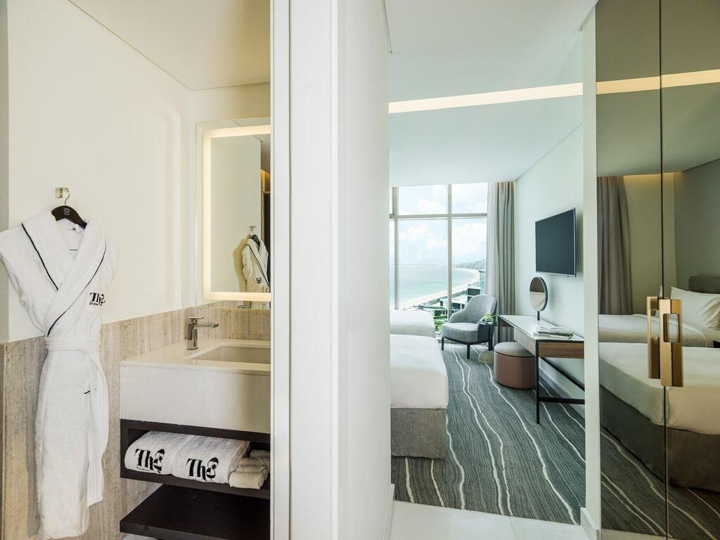 A hotel room with a bathroom, a bed, a desk, and a view of the sea.