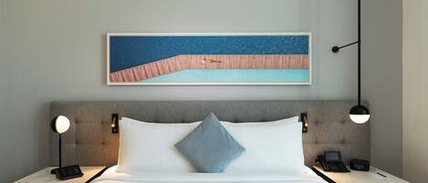 A hotel room with a bed, a nightstand with a phone, a lamp, and a painting on the wall.