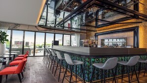 A modern bar area with a high ceiling, bar stools, and a view of the city through large windows. - Th8 Palm Dubai Beach Resort, Vignette Collection (Dubai)