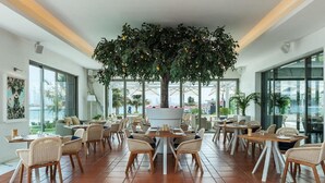 A modern dining area with a central tree, multiple tables, and chairs. - Th8 Palm Dubai Beach Resort, Vignette Collection (Dubai)
