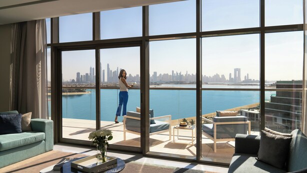A spacious living room with a large window overlooking a city skyline and water. - Th8 Palm Dubai Beach Resort, Vignette Collection (Dubai)