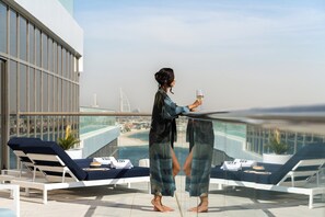 Un balcón con sillones de descanso, barandilla de vidrio y vista al mar.