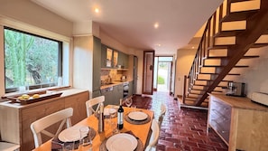 A dining area with a wooden table set for four, a kitchen with a built-in oven, and a staircase with wooden steps.