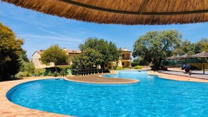 A swimming pool with a curved design, surrounded by a brick deck and a thatched roof structure.