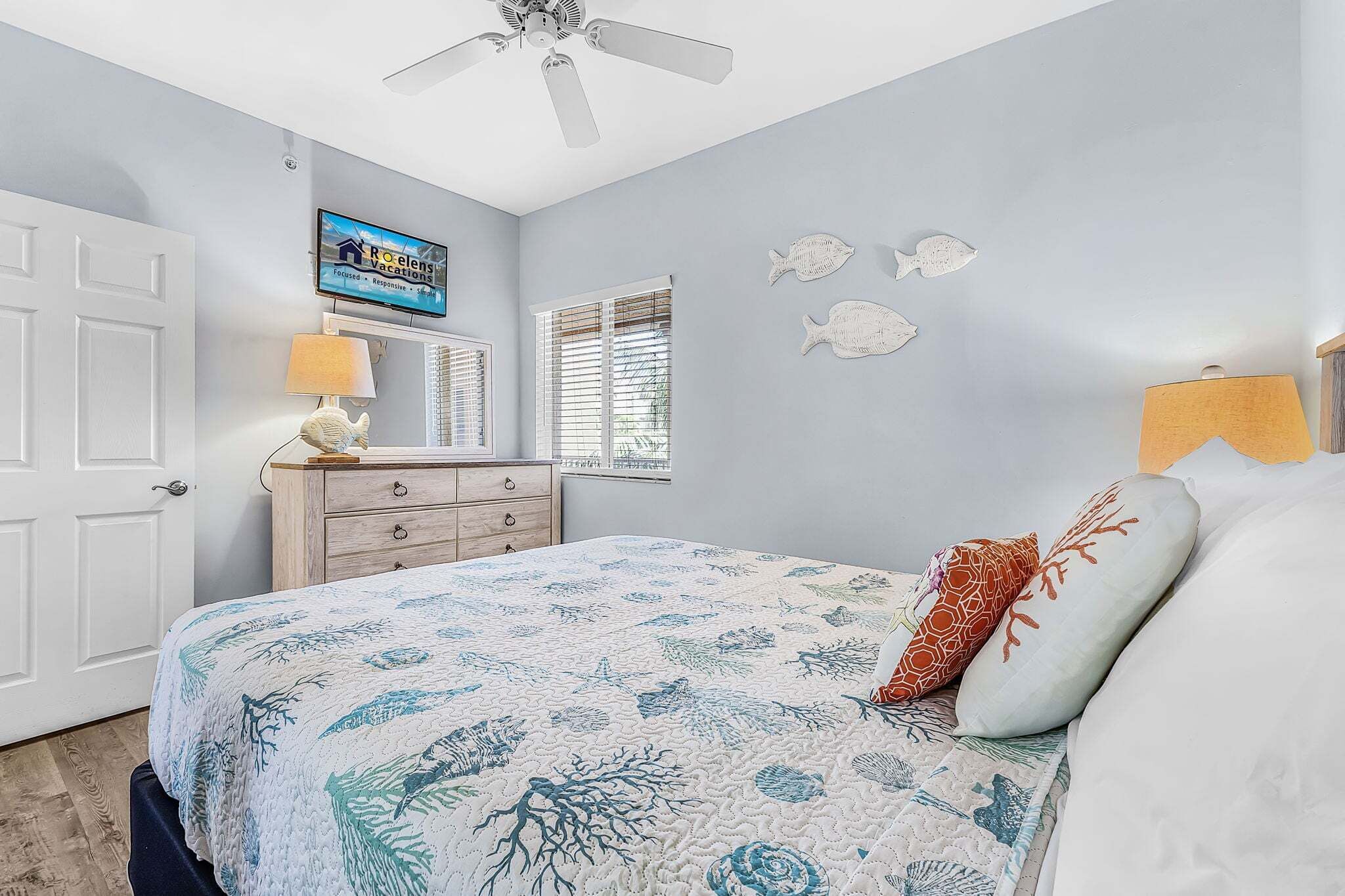 Une chambre à coucher comprenant un lit, un ventilateur de plafond, une commode, un téléviseur et des éléments décoratifs sur les murs.