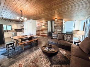 A spacious living area with a wooden ceiling, a sofa, a coffee table, and a rug. - New | 5 Min to Glacier | Hot Tub & Fire Pit (Martin City)